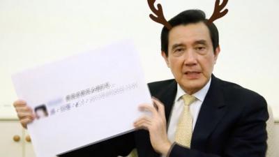 Former Taiwanese President Ma Ying-jeou holding a copy of a Facebook post about him, while a cartoon animation of antlers protrude from his head