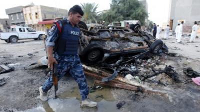 An Iraqi policeman walks past the site of a car bomb attack in Samawa