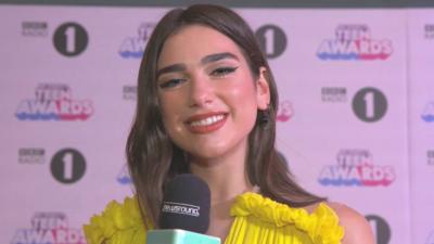 Dua Lipa smiles while holding a microphone at the Radio 1 Teen Awards.