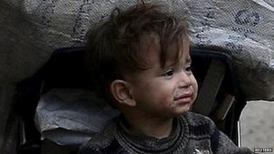 A child rests inside a pushchair filled with cartons collected to use for heating in the town of Douma, Eastern Ghouta in Damascus, Syria