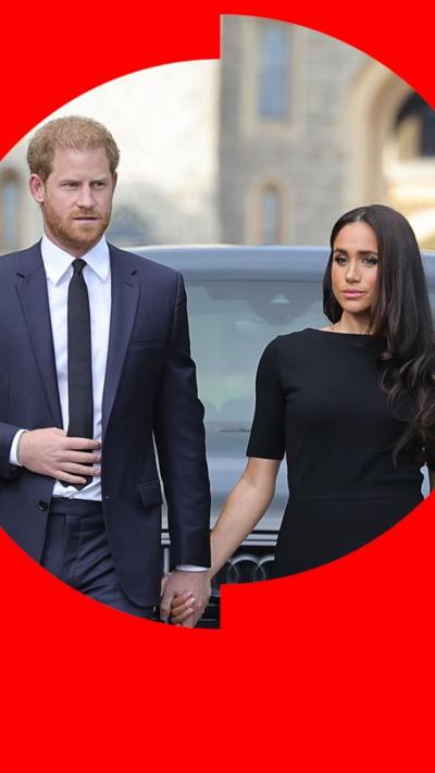 Harry (left), wearing a suit, holds hands with Meghan (right) who is wearing a black dress.