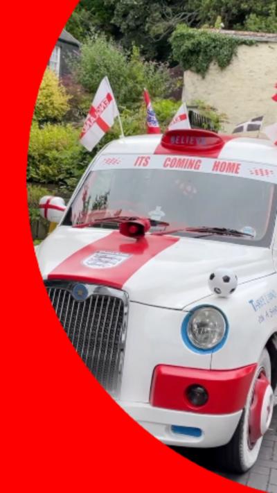 A white and red car which has "its coming home" written in red letters. There are english flags and footballs over the car. The number plate is blurred.