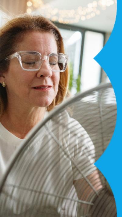Woman with glasses sits infant of an electric fan.