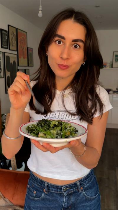 A woman with long dark hair wearing a white t-shirt and blue jeans holds a bowl of food