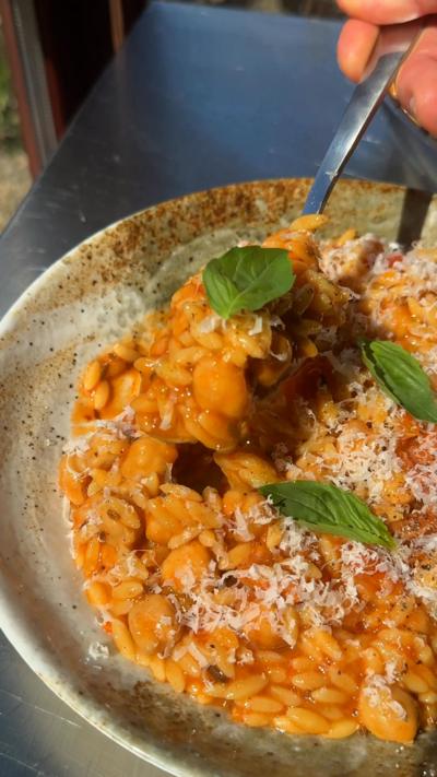 A stoneware bowl filled with tomato orzo with chickpeas and basil leaves on top.