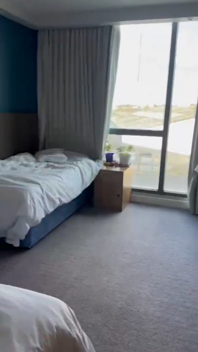 Phone footage of a hotel room showing a single bed with white sheets next to a window.