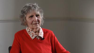 Olga Henderson wearing a red jumper looking off camera being interviewed about her WW2 experience