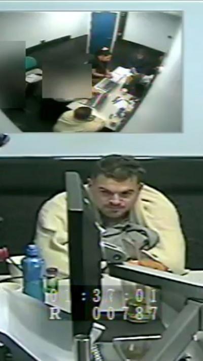 A man with dark hair in a cream jacket sat in a police interview room