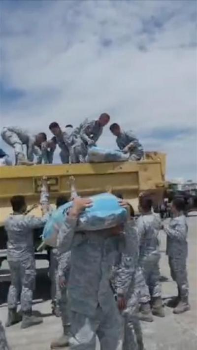 People dressed in camouflage load a bag from a yellow truck.
