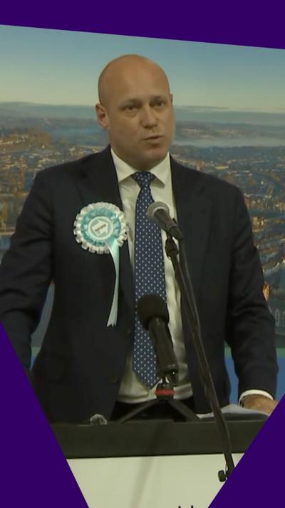 Dan Thomas in a suit and wearing a rosette 