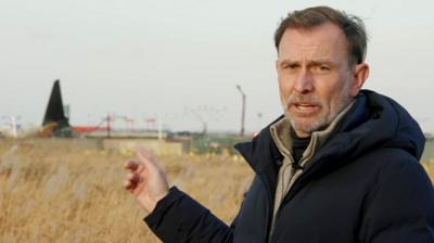 Rupert Wingfield-Hayes pointing at a crashed plane.