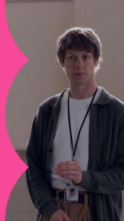 A man in a cardigan stands in a dimly lit classroom in a prison