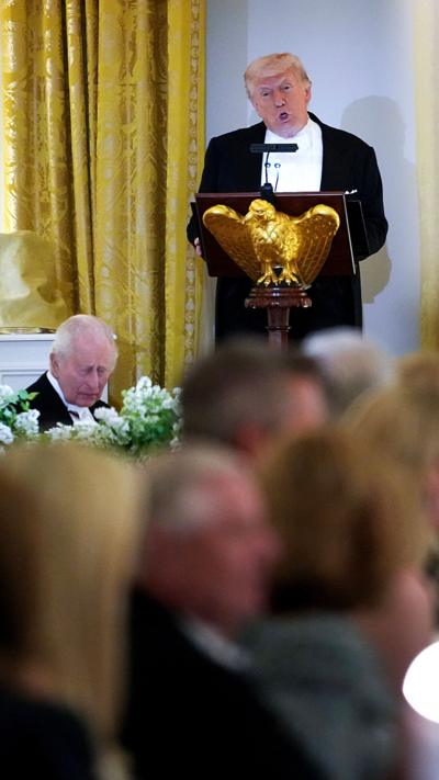 Donald Trump, dressed in a tuxedo, stodd at a lectern, with King Charles seated to the left