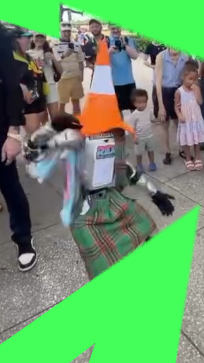 Composite image of a robot wearing traffic cone hat and kilt dancing among a crowd