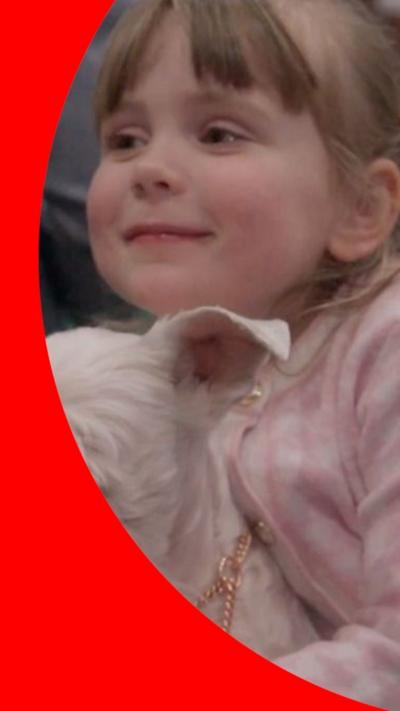 Four year old Caitlyn who has light hair and is wearing a pink jacket, holding a white dog with a beard