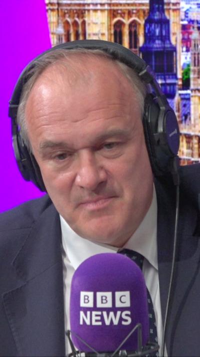 Sir Ed Davey wears headphones and sits in front of a microphone in a radio studio.