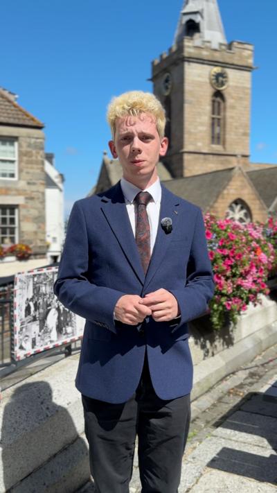 A man with blonde hair wearing a blue suit looking at the camera