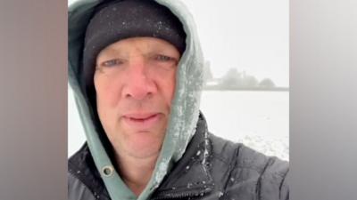 A man with a black wooly hat and a green hood standing in the snow