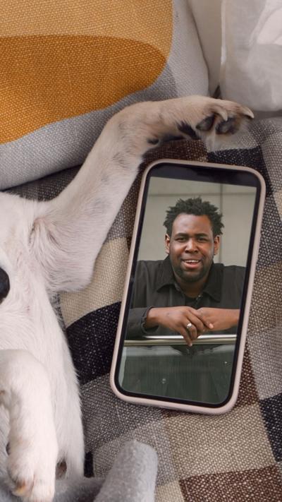 A man is seen on a phone screen being held by a dog