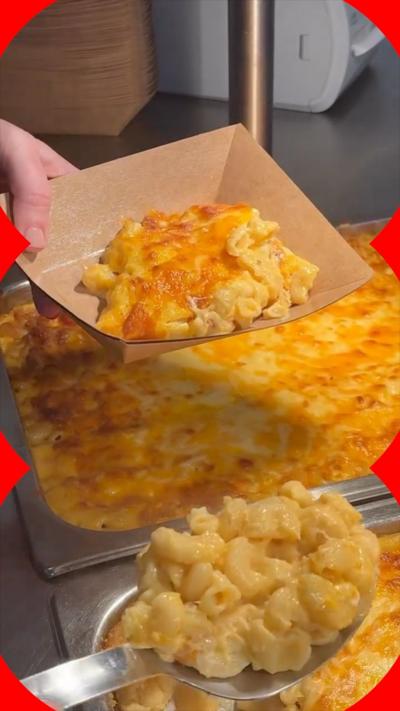Macaroni cheese being spooned into a cardboard rectangle bowl. 