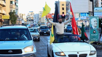 A man holds a Hezbollah flag while standing in a car, at the entrance of Beirut's southern suburbs