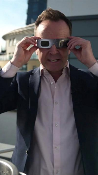 A man holds solar eclipse glasses up to his eyes