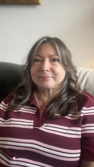 a woman sitting on a sofa. She is wearing a striped top and has long curled hair. 