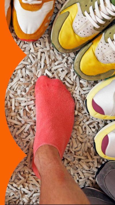 A pair of feet in red socks, surrounded by a circle of colourful trainers, viewed from above,