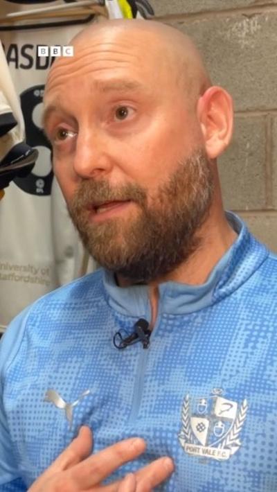 A bald man with a beard in a sky blue football shirt