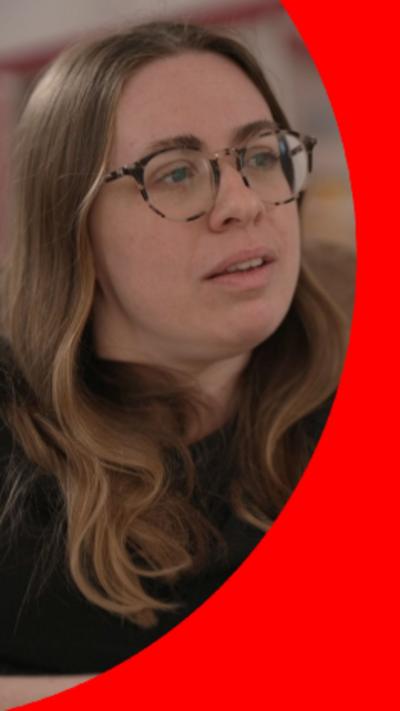 A woman with long brown hair and glasses, wearing a black top.