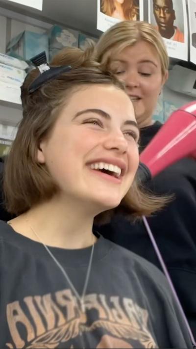 A girl laughs as she is having her hair done, behind the scenes of Malory Towers with the main star, Ella.