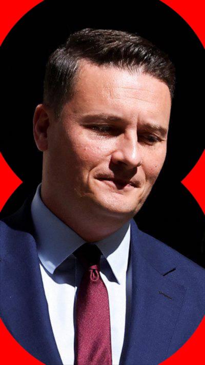 Wes Streeting looks down. He is wearing a blue blazer and shirt and tie. 
