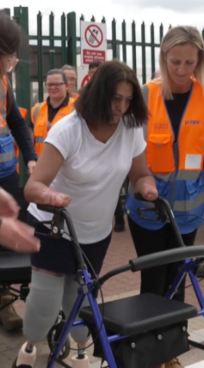 A woman with no hands or feet walks with the aid of a frame and supported by two women