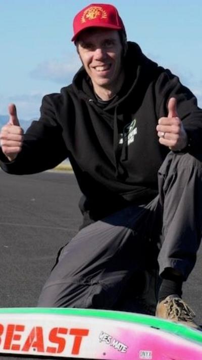 Man with red cap and black hoodie showing thumbs up next to a radio controlled car