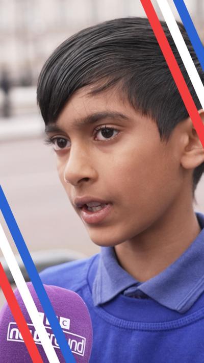 A boy wearing a blue jumper speaking into a Newsround microphone on the Mall