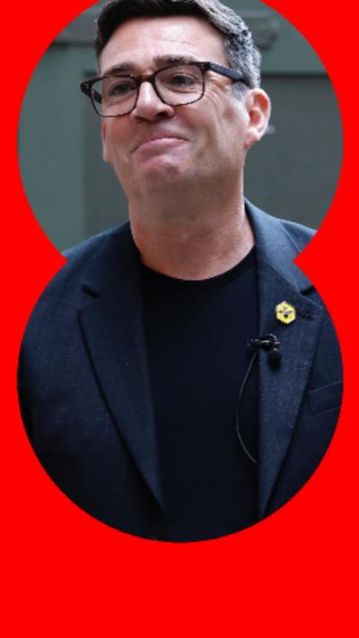 Andy Burnham has short dark hair, glasses and is wearing a navy blazer with a small yellow badge.