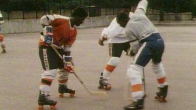 Three men playing street hockey, on rollerskates.