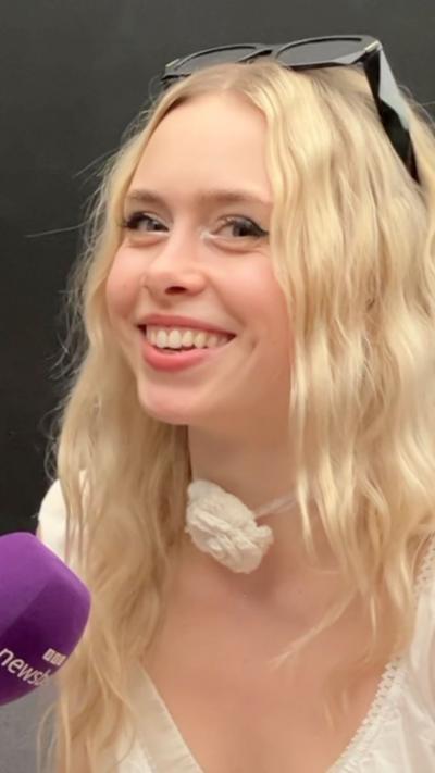 Singer Erin LeCount with wavy blonde hair wearing white blouse and necklace with a white flower