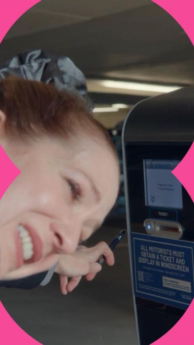 Character Rachel grimaces as she tries to reach a car park ticket machine using a pen