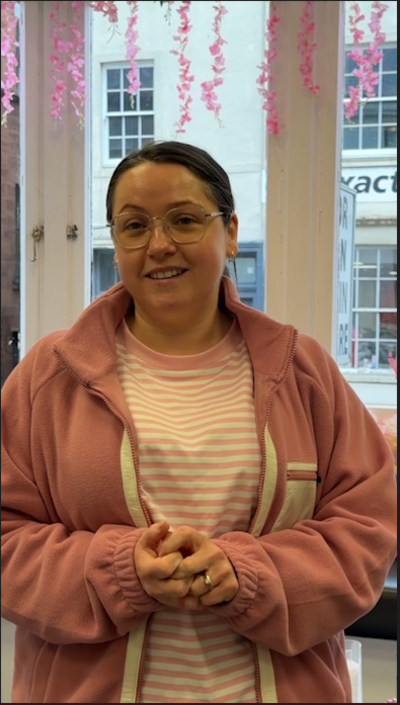 Woman with a pink striped top and pink jacket in front of a shop window.