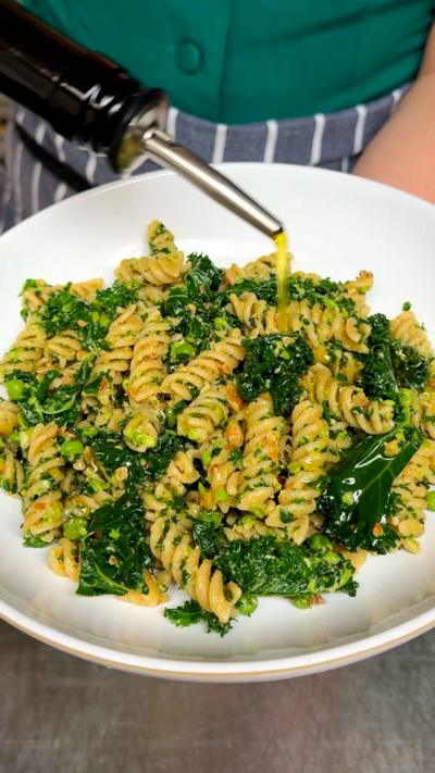 A white plate of pasta salad with kale and peas