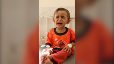 A toddler in orange Spider-Man pyjamas sits on a bed crying