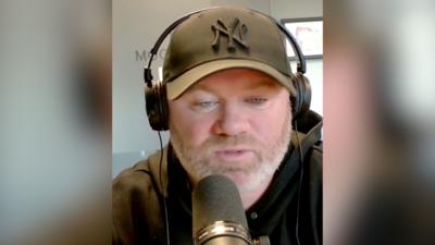 Wayne Rooney in a hoodie and baseball cap wearing headphones and sitting behind a mic