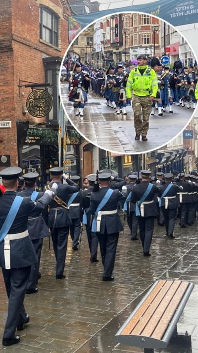 Military personnel walk through a city street saluting in rainy weather.