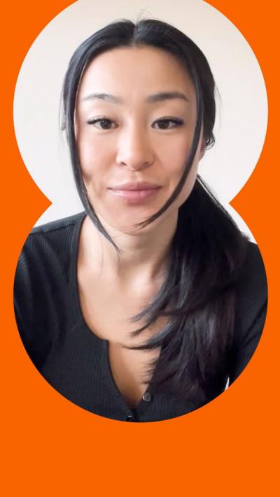 A woman with long black hair looks into the camera. She wears a black top