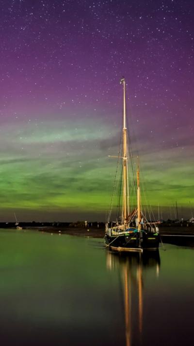 Northern light over Blakeney Harbour with a sail boat in the water that is reflecting the aurora