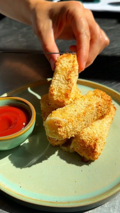 A green plate with mozzarella sticks on it and a small bowl of sauce, with a hand dipping one in
