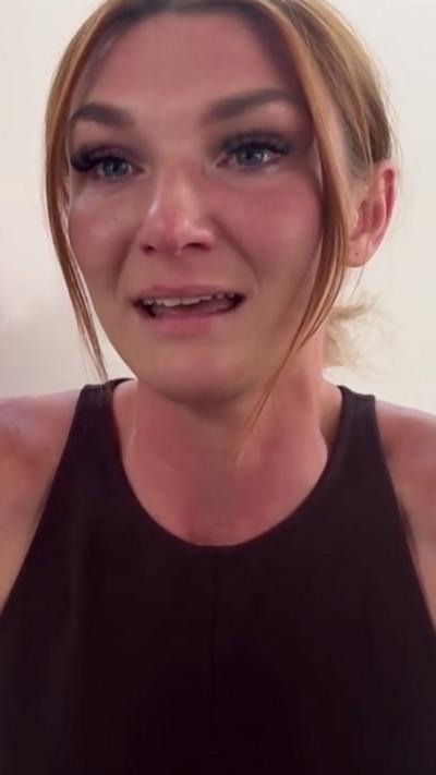 A young woman crying, with hair tied back, wearing a black tank top 