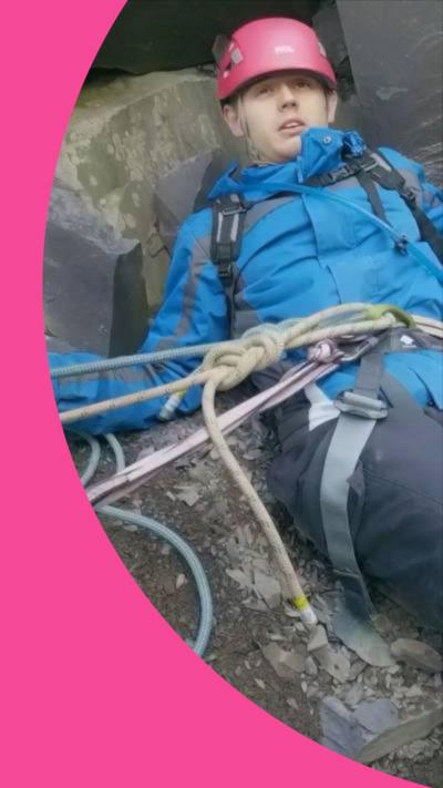 A man in climbing gear lies on rocks - he is attached to multiple ropes 