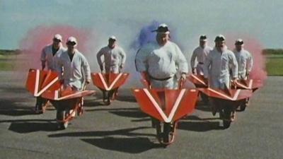 Members of the Red Barrows carrying out a display, wearing white flight suits and pushing red wheelbarrows.